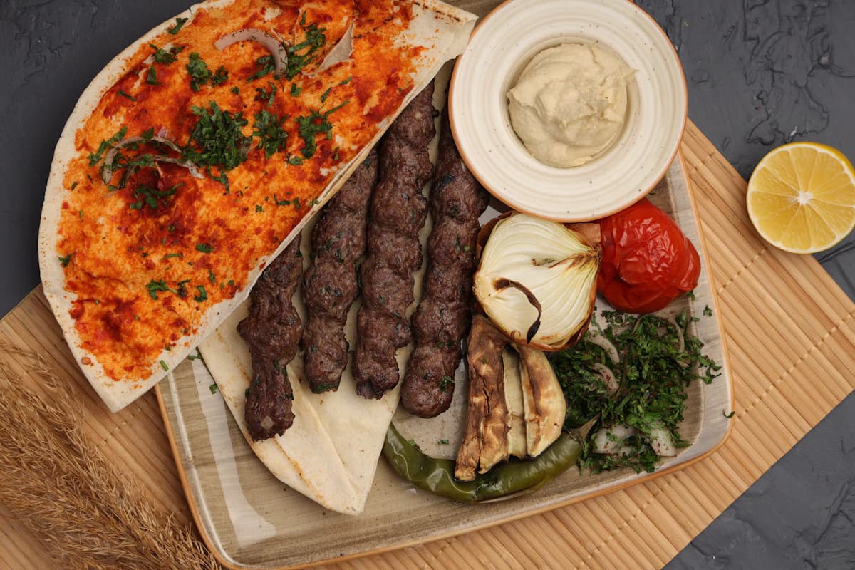 Kofta kebab skewers on flatbread with hummus and grilled vegetables