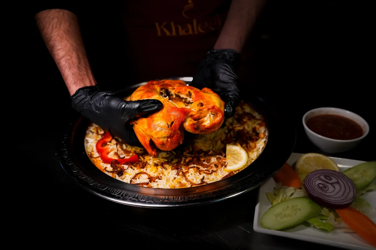 A Khaleej Mandi chef serving a whole roast chicken on mandi rice